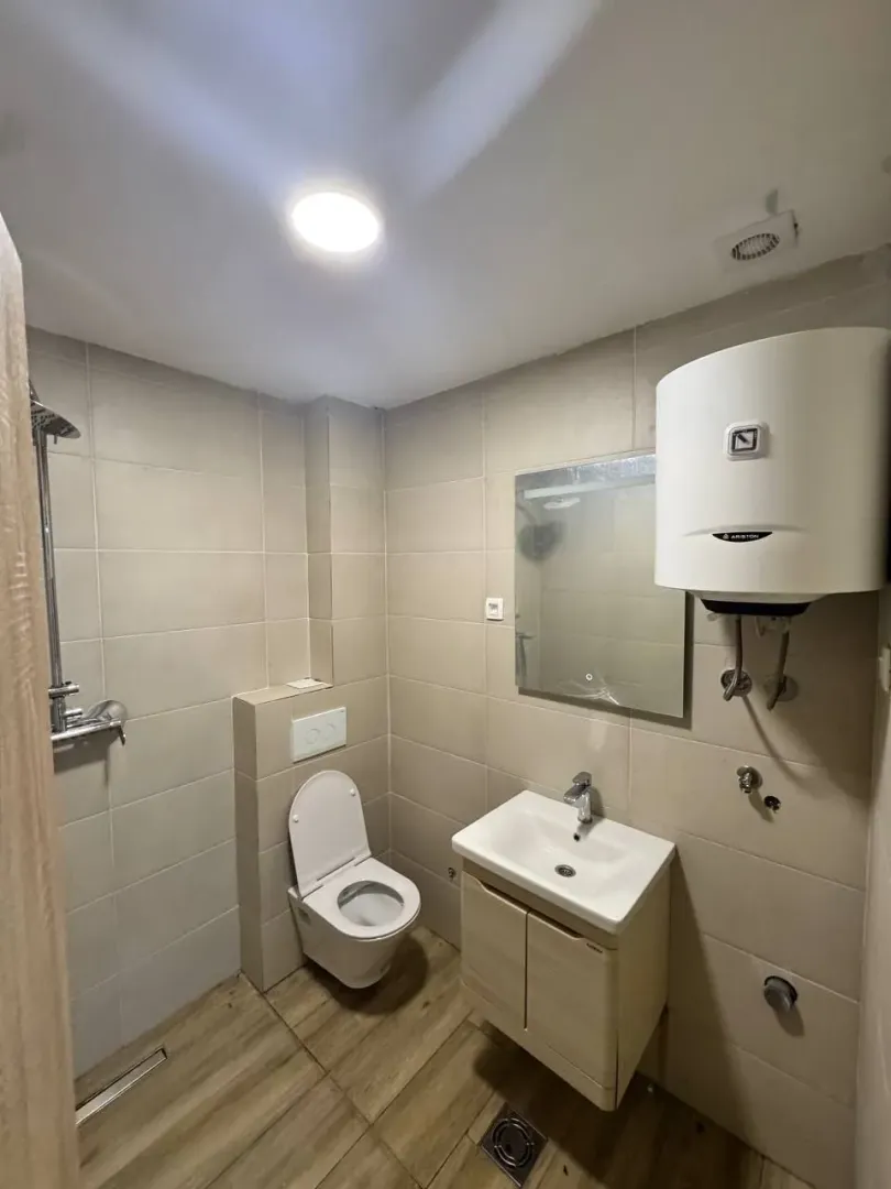Manje kupatilo obloženo keramičkim pločicama sa tuš kabinom, umivaonikom i wc šoljom.
