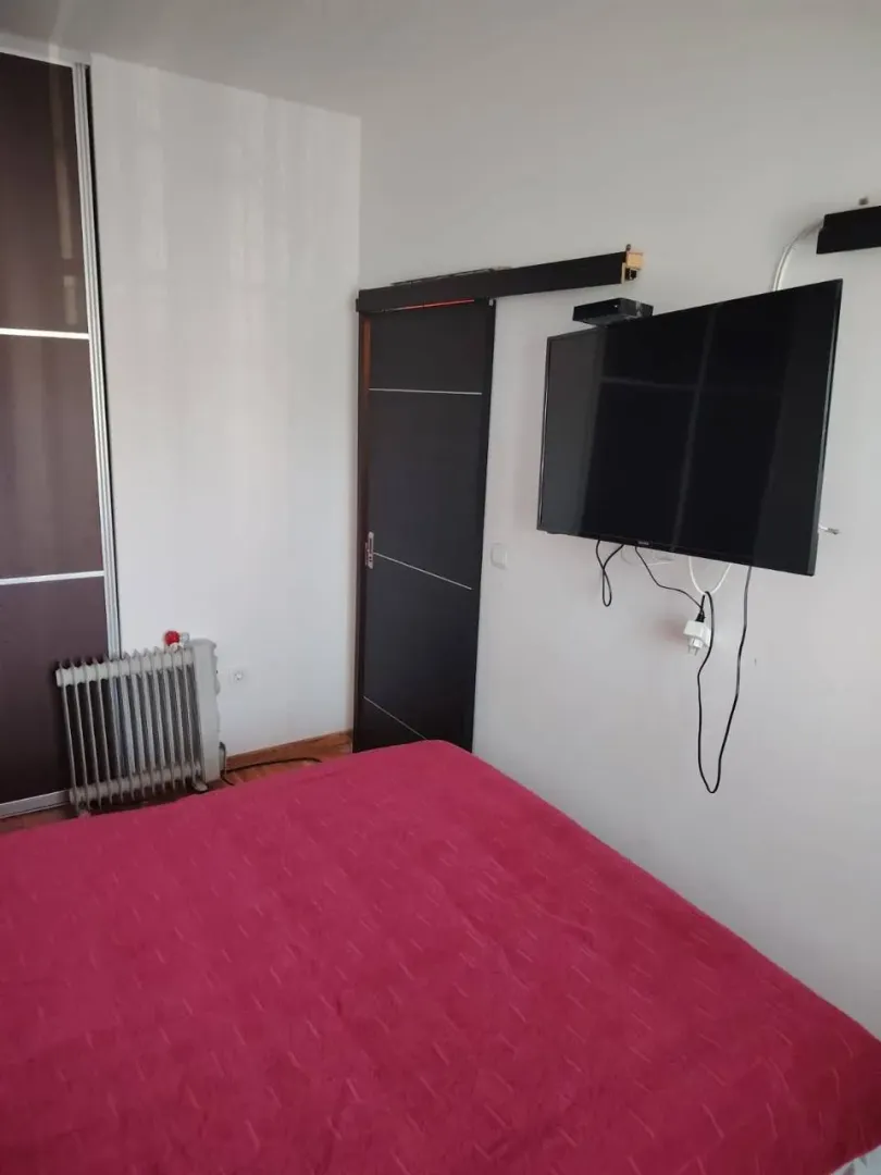 Spavaća soba sa krevetom, plakarom i televizorom na zidu.
