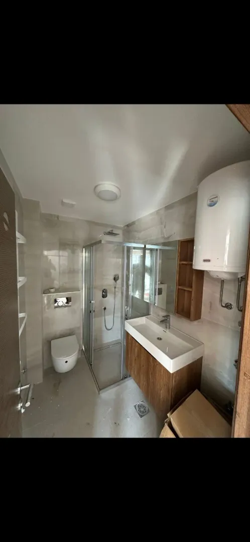 Moderno opremljeno kupatilo sa tuš kabinom i belom sanitarijom.