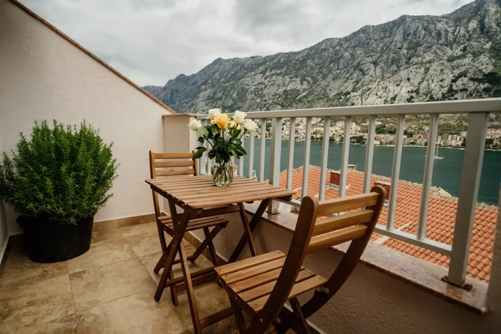 Namješten balkon sa drvenim stolom, stolicama i pogledom na more i planine.