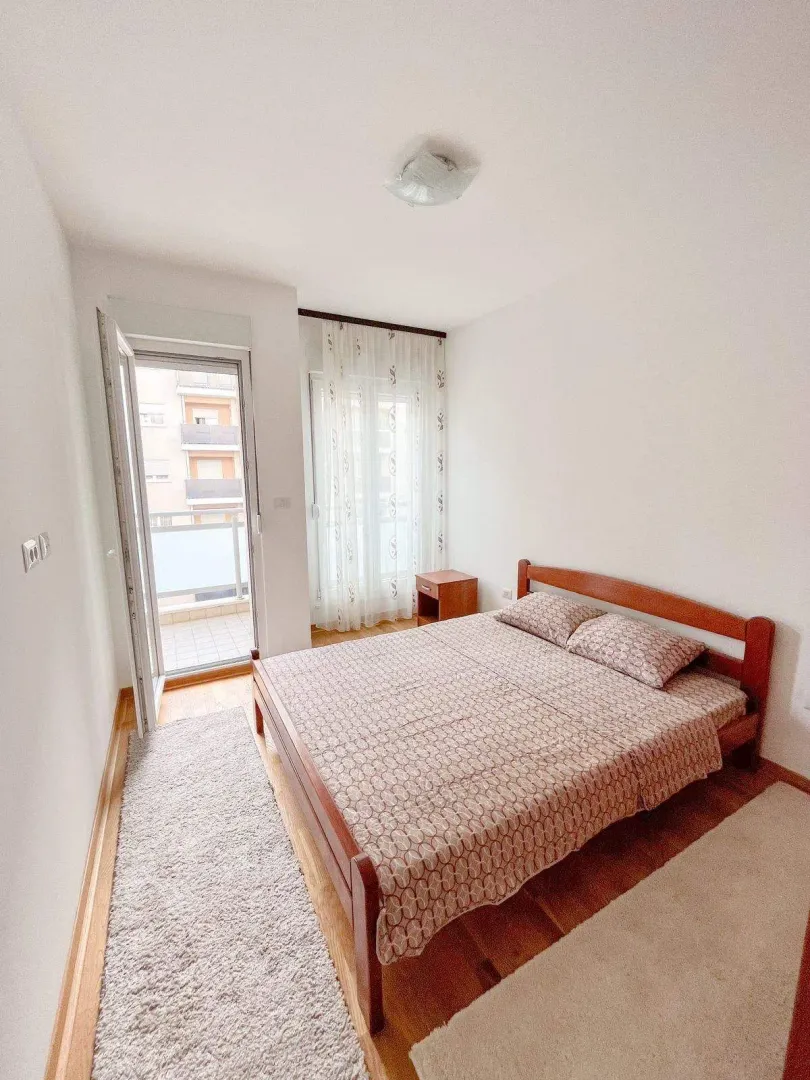 Svijetla spavaća soba sa drvenim krevetom i izlazom na balkon.