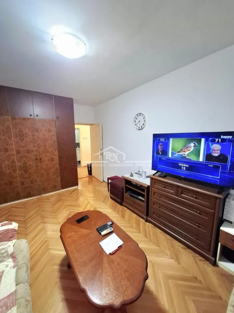 Dnevna soba sa drvenim nameštajem, televizorom i parketom na podu.