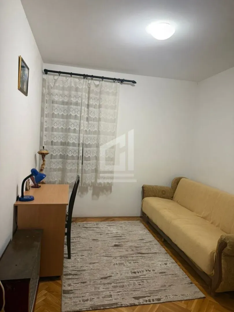 Small room with a sofa, a desk, and a window with curtains.