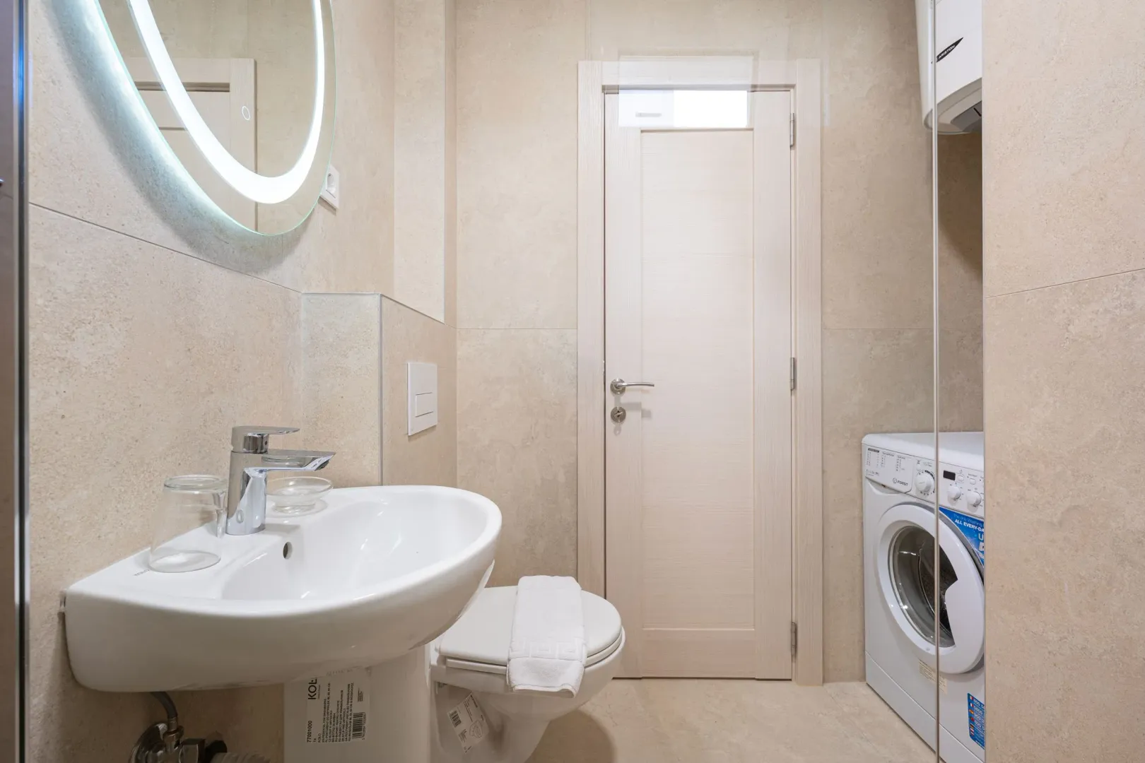 Modern bathroom with a sink, toilet, washing machine, and mirror.