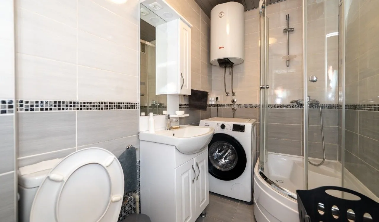 Compact bathroom with a shower cabin, washbasin, washing machine, and water heater.