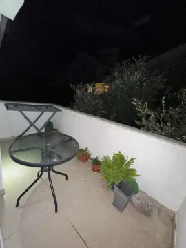 Manja terasa sa stolom, stolicama i saksijama sa cvećem noću. - image 9