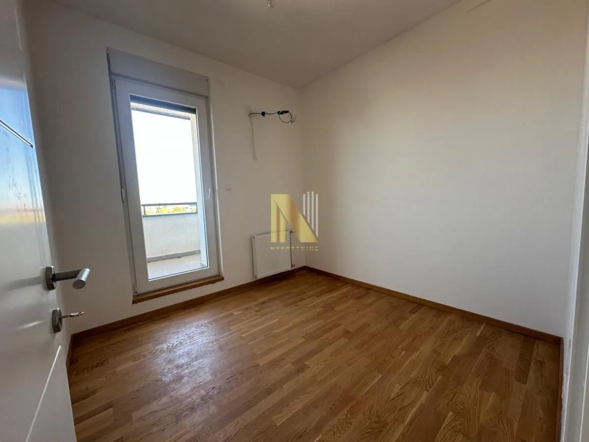 Prazna soba sa parketom i izlazom na balkon.