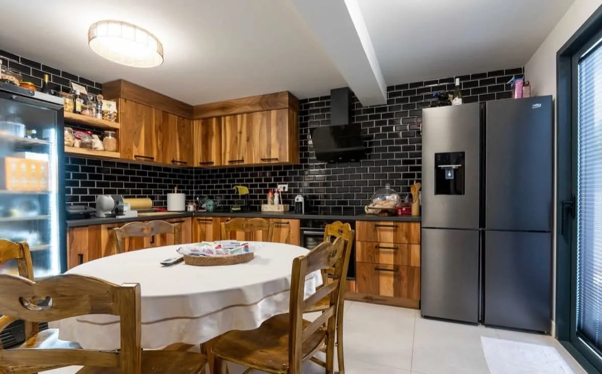 Spacious kitchen with wooden cabinets, black tiled backsplash, and a dining table in the middle.