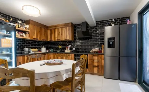 Spacious kitchen with wooden cabinets, black tiled backsplash, and a dining table in the middle. - image 7