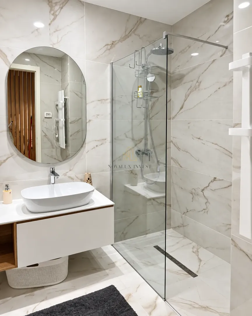 Modern bathroom with a walk-in shower, washbasin, and round mirror.