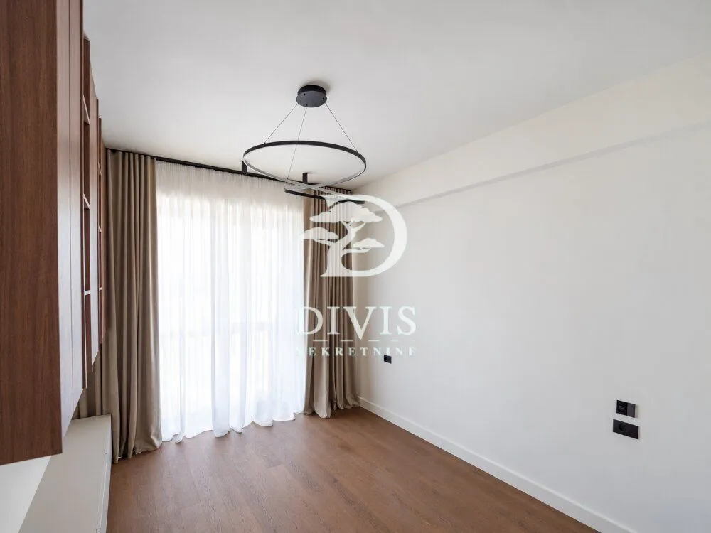 Empty room with wooden flooring, curtains and a modern chandelier.