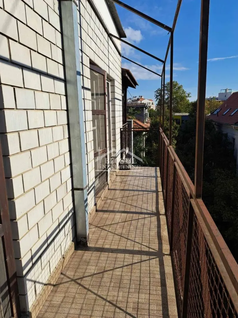 Dugački popločani balkon sa metalnom ogradom i pogledom na okolinu.