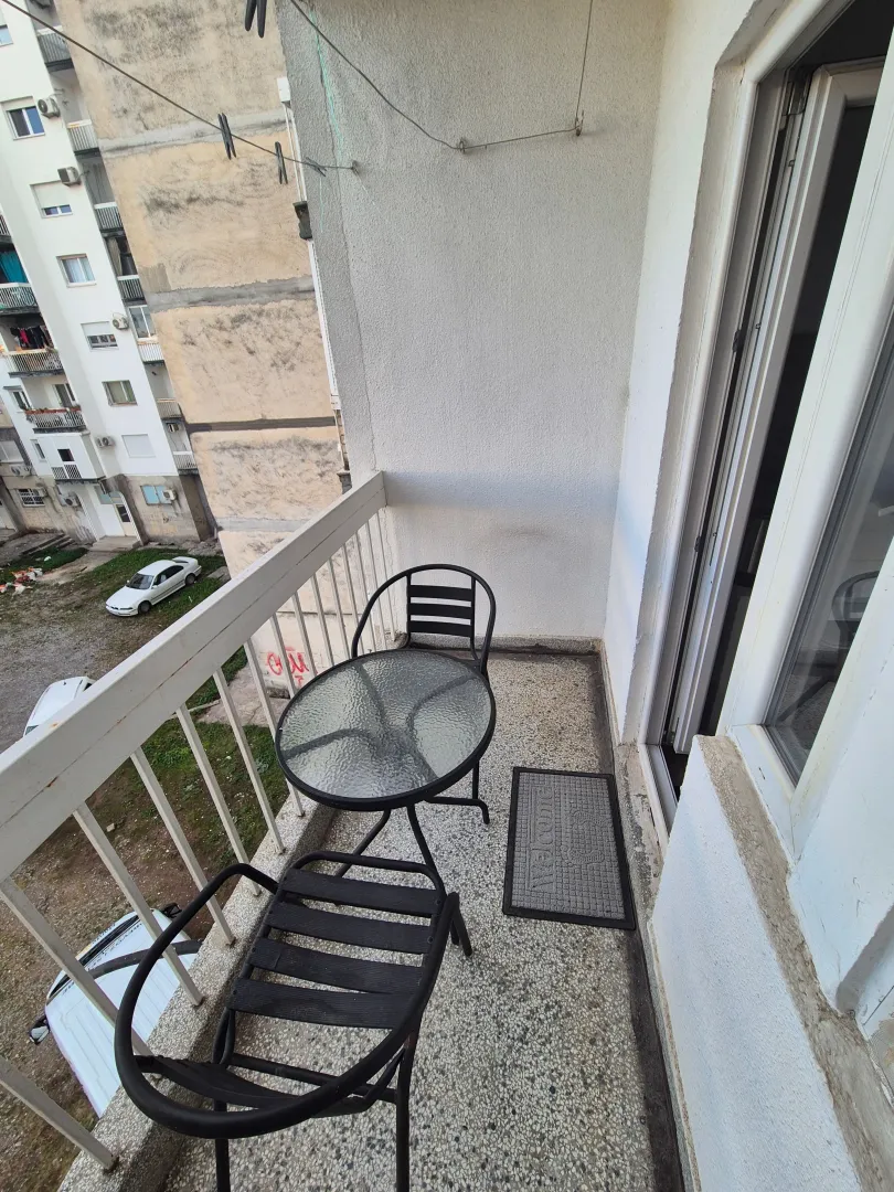 Small furnished balcony with a table and two chairs overlooking buildings.