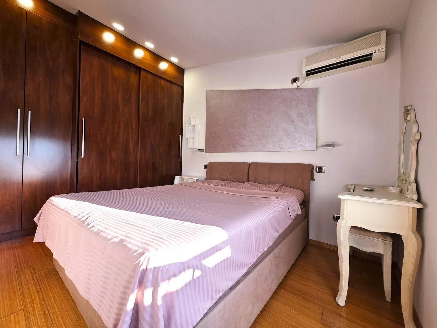 Furnished bedroom with a large double bed, wooden wardrobe, and air conditioning.