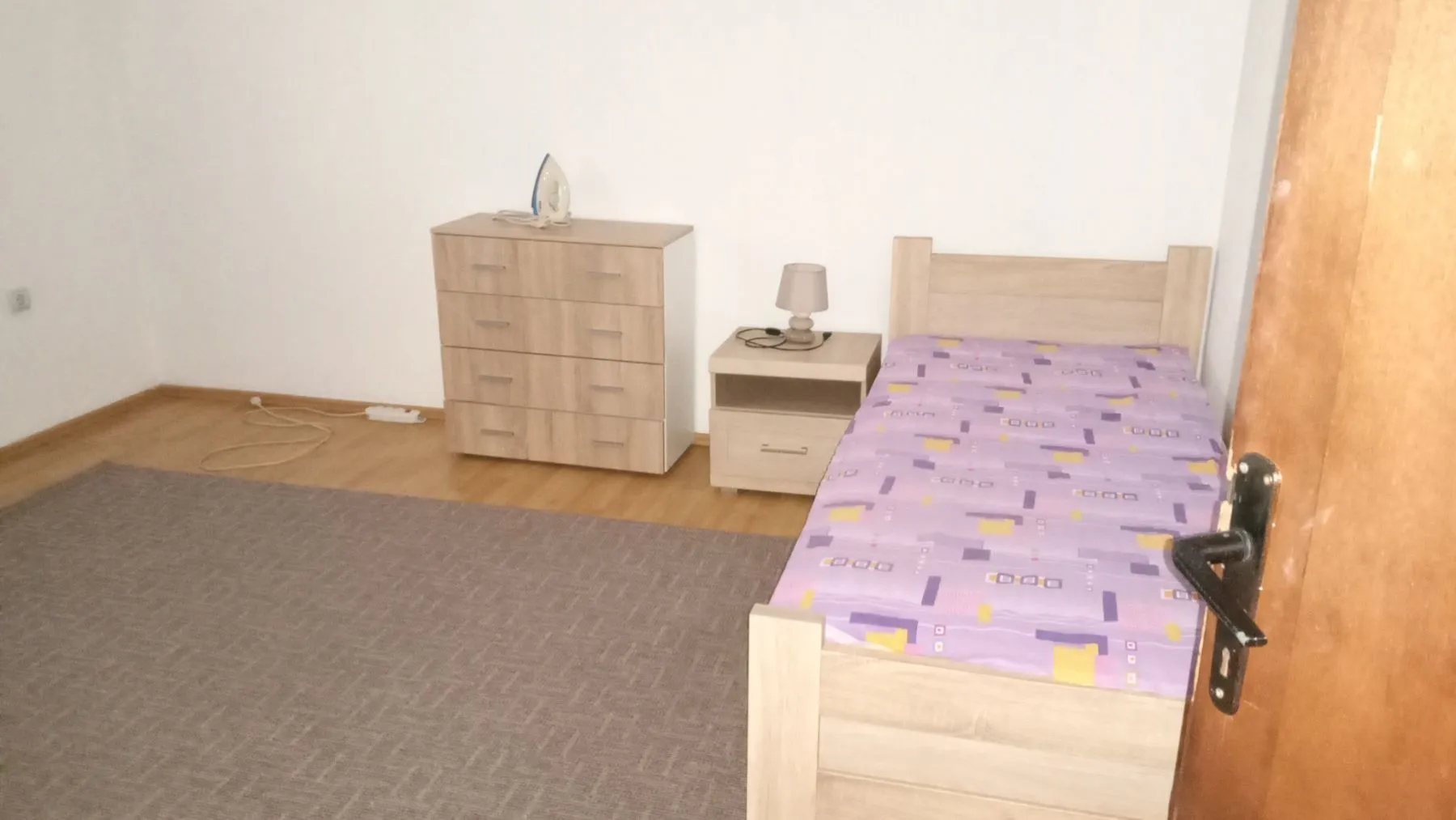 A simple bedroom featuring a single bed, a chest of drawers, and a nightstand.