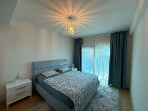 Spavaća soba sa velikim bračnim krevetom, bijelim noćnim stočićem i zavjesama na prozorima. - image 8