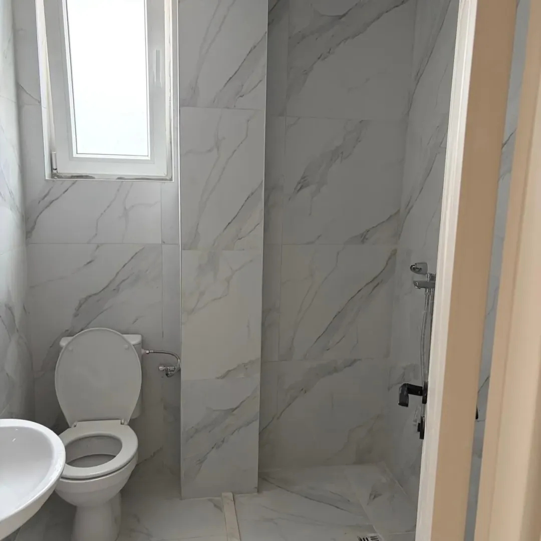 Smaller bathroom tiled with marble tiles, featuring a toilet, sink, and shower.