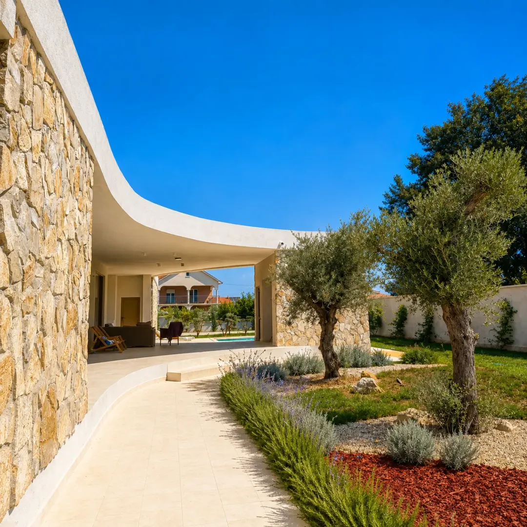 Exterior of the house with a paved pathway, landscaped yard, and olive trees.