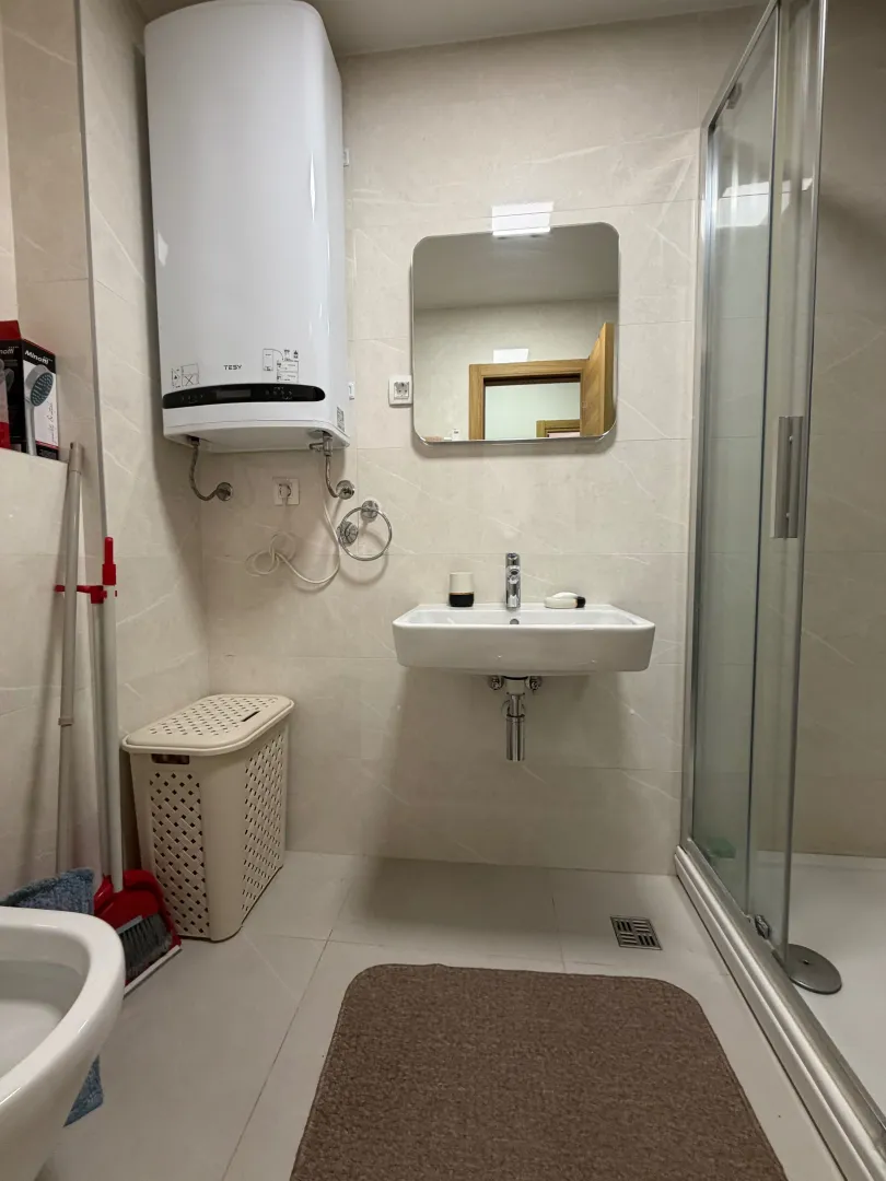 Bathroom with a washbasin, mirror, shower cabin, and water heater.