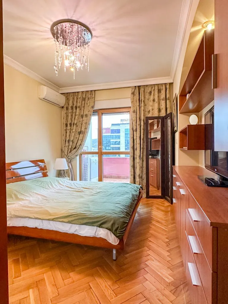 Furnished bedroom with a double bed, wooden parquet flooring, and access to the terrace.