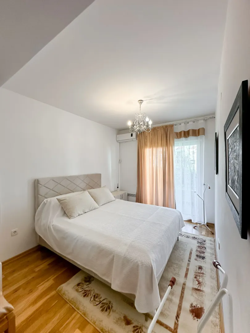 Bright bedroom with a double bed, wooden flooring, and balcony doors.