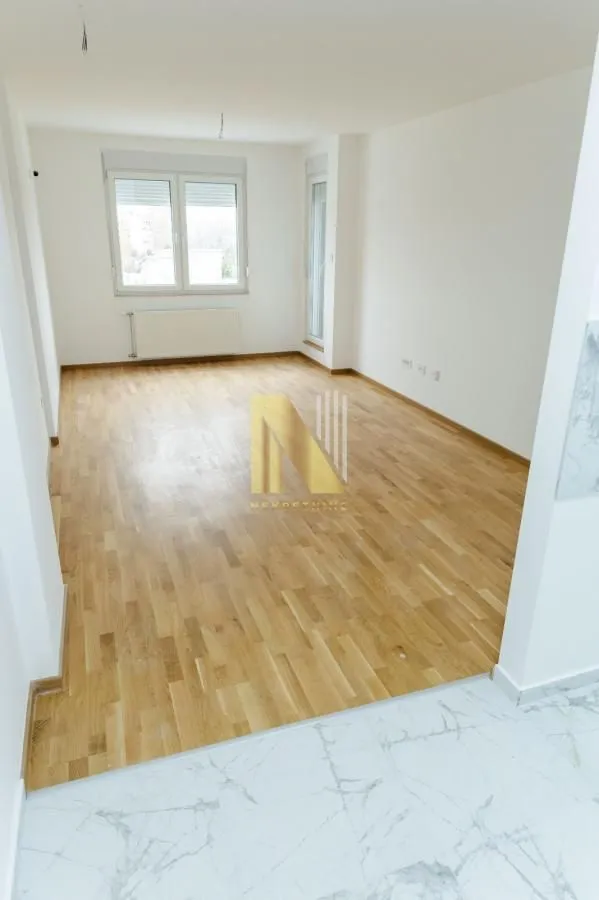 Prazna soba sa parketom i belim zidovima.