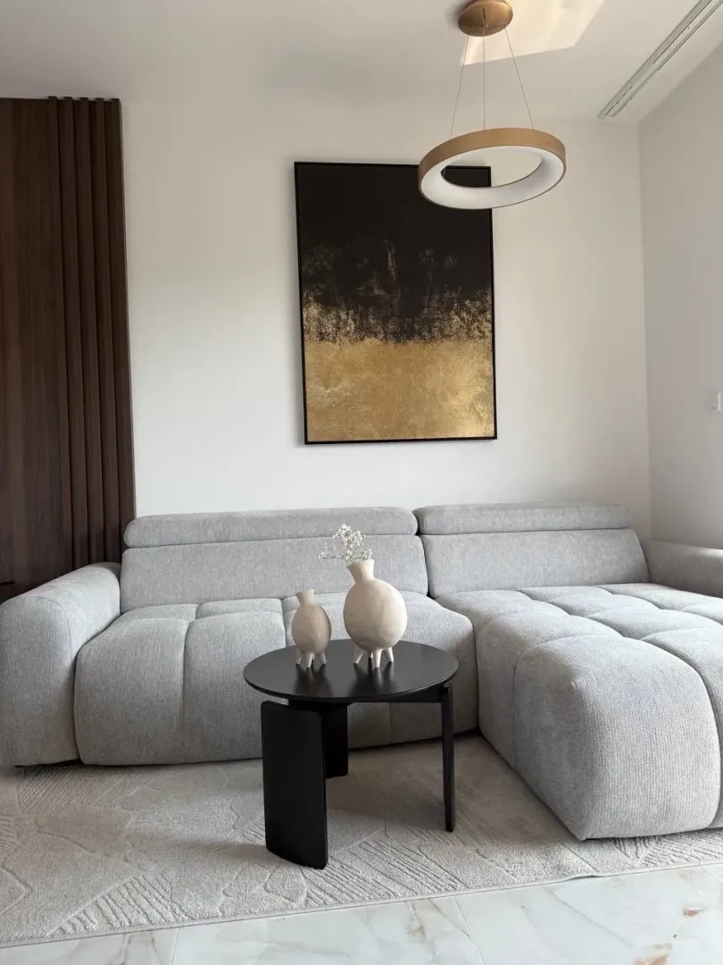 Dnevna soba sa sivom ugaonom garniturom, crnim stočićem i modernim lusterom.