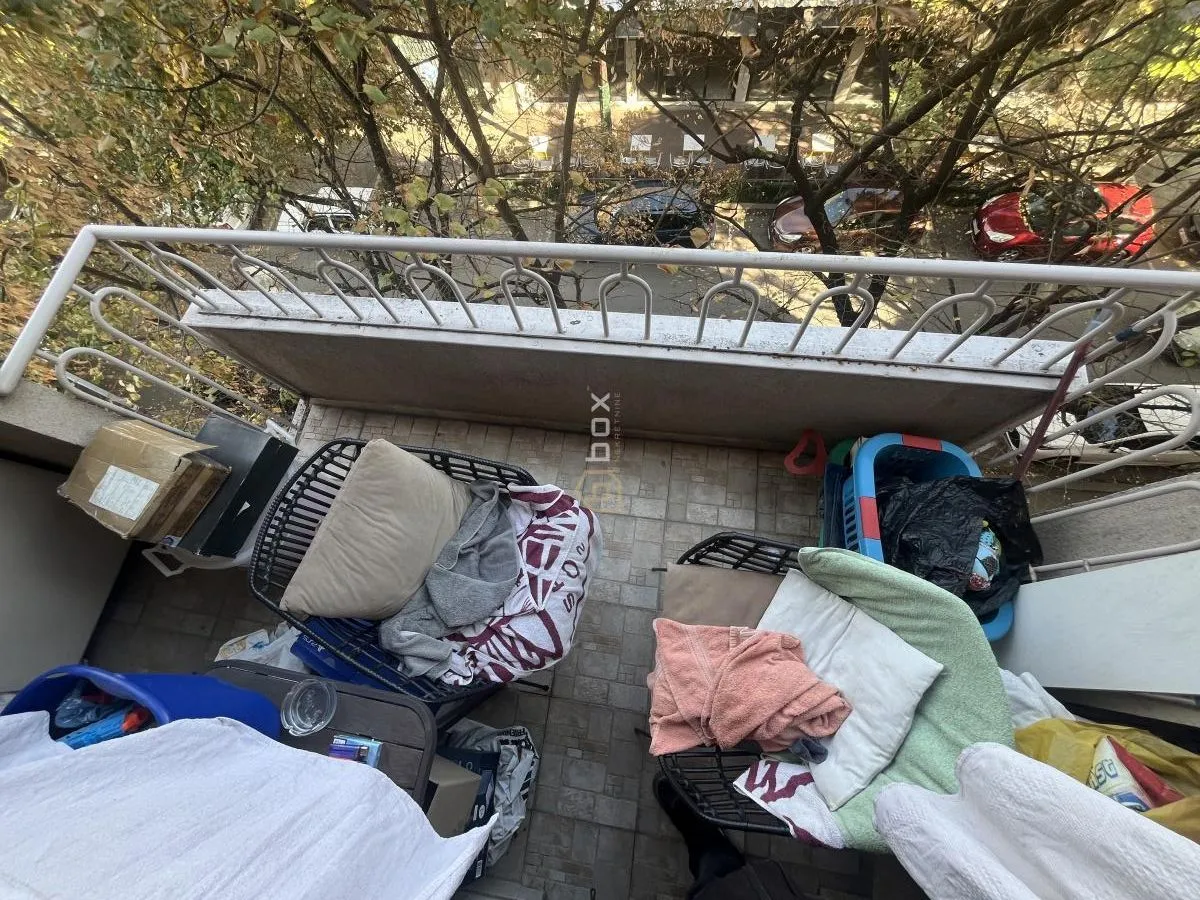 Manji namešten balkon sa pogledom na ulicu i drveće.