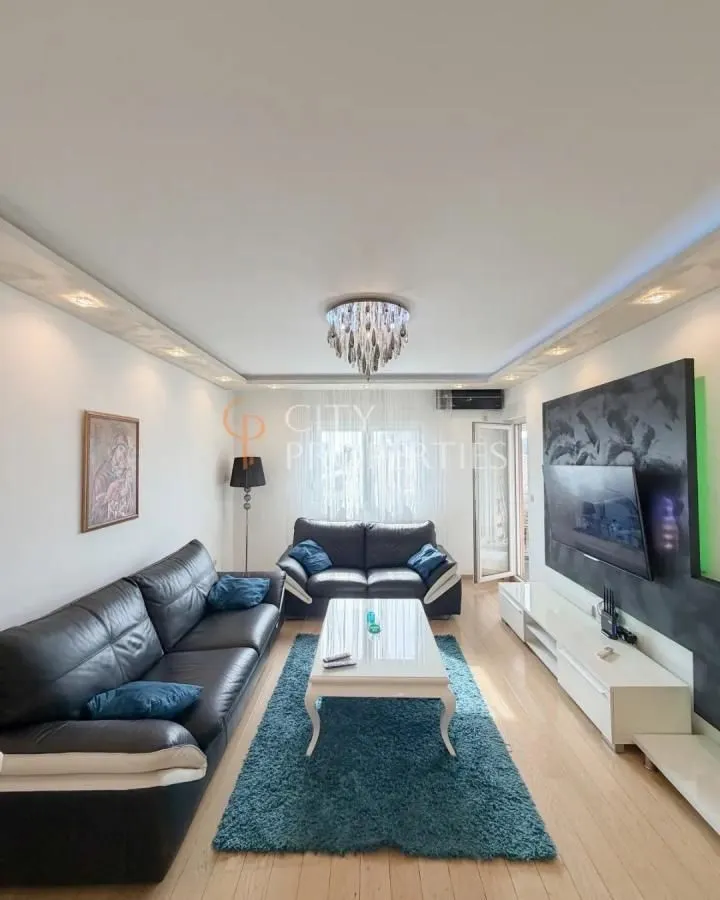 Spacious living room with black leather sofas and a TV unit.