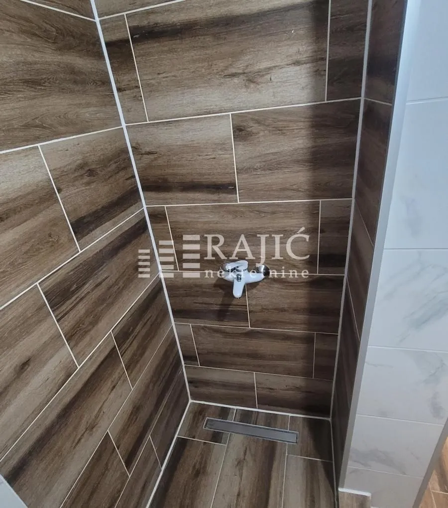 Prikaz tuš kabine obložene pločicama sa dezenom drveta.