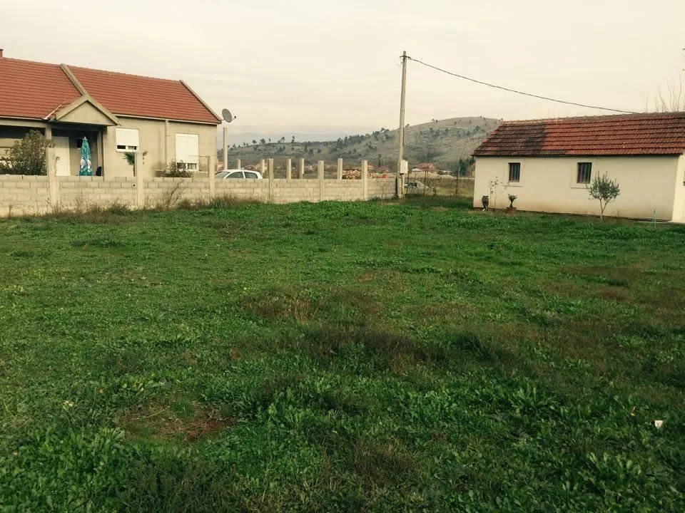 Travnato dvorište sa kućom i pomoćnim objektom u pozadini.