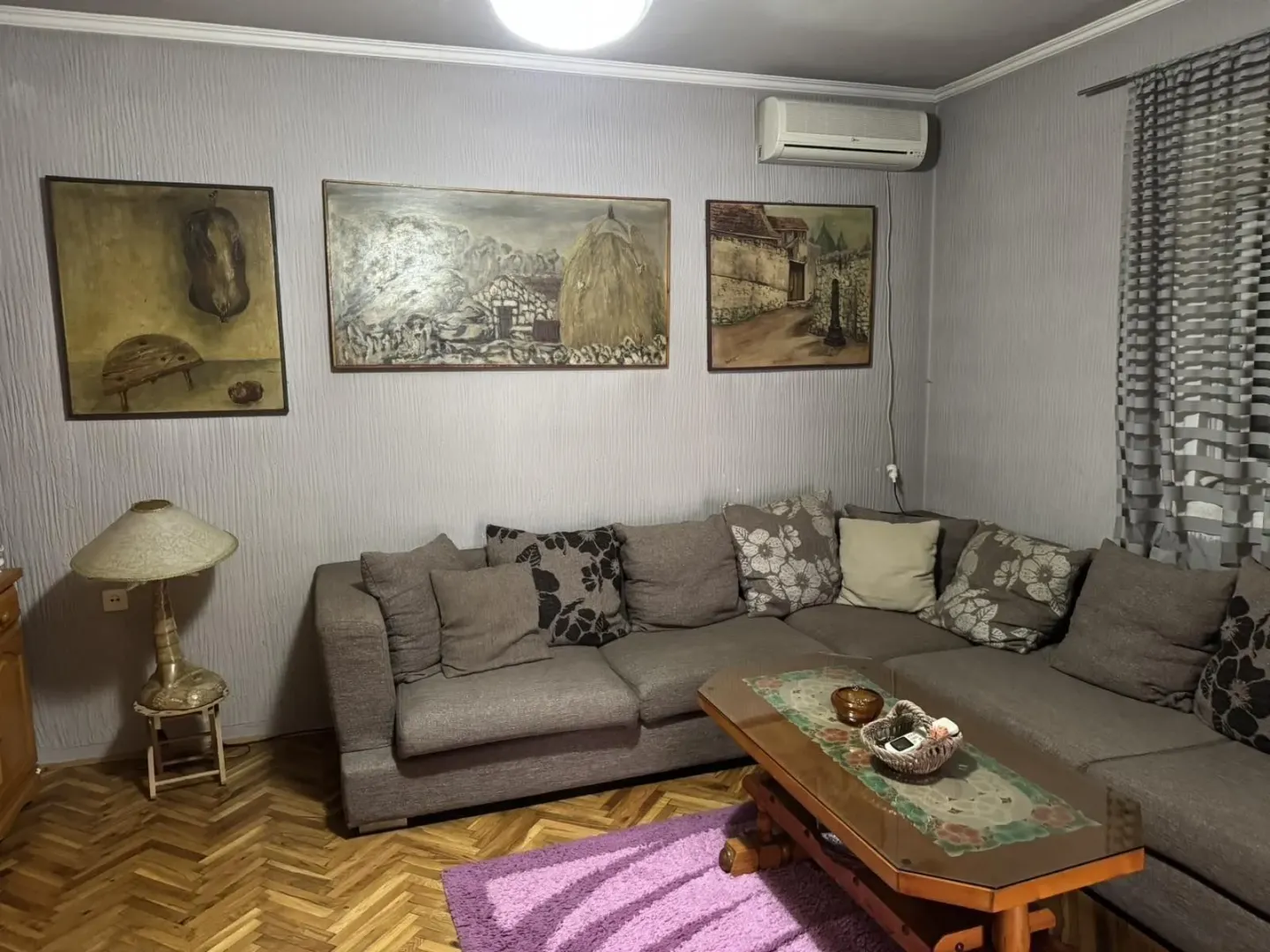 Dnevna soba sa velikom ugaonom garniturom, klub stolom i umjetničkim slikama na zidu.