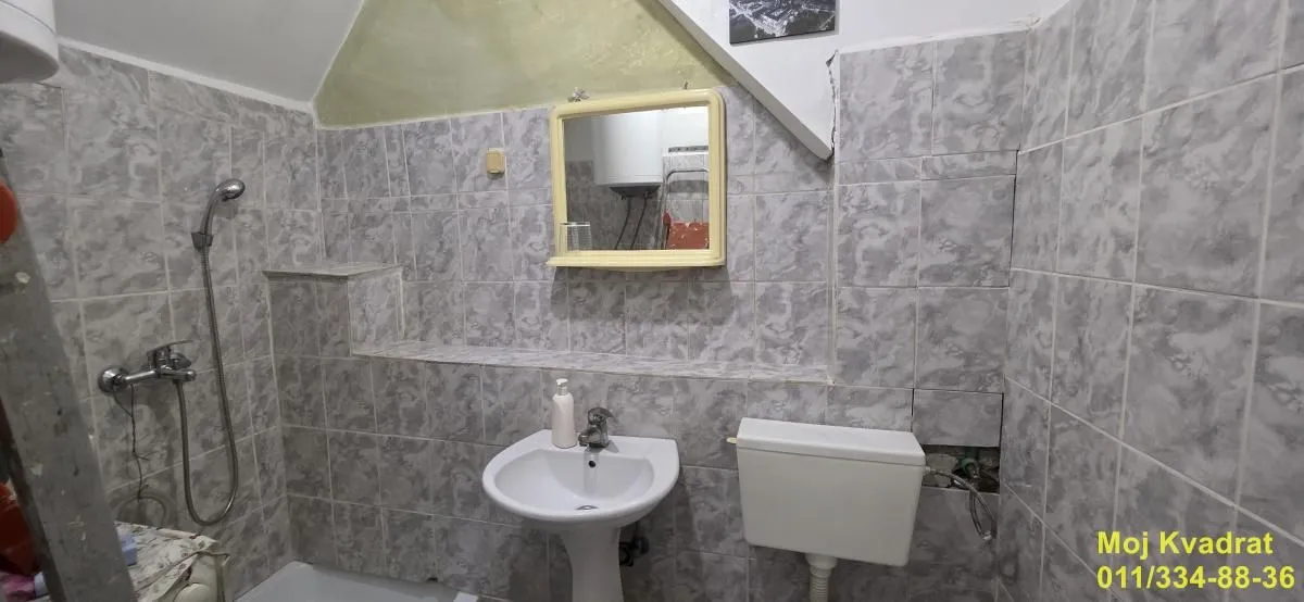 Kupatilo obloženo keramičkim pločicama sa umivaonikom, ogledalom i WC šoljom.