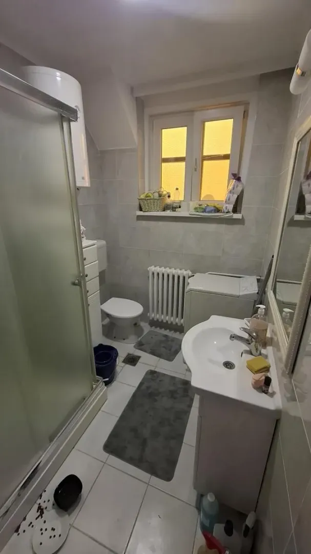 Manje kupatilo sa tuš kabinom, umivaonikom, WC šoljom i prozorom.