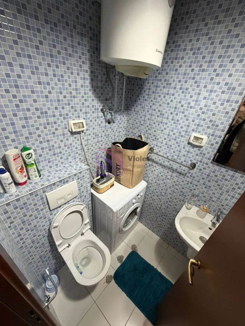 Smaller tiled bathroom with a toilet, washbasin, and washing machine.