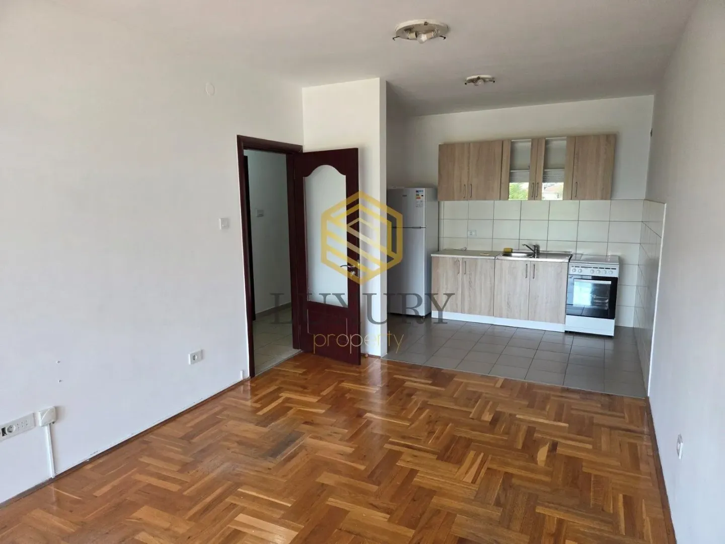 Living room with parquet flooring and kitchen in the background.