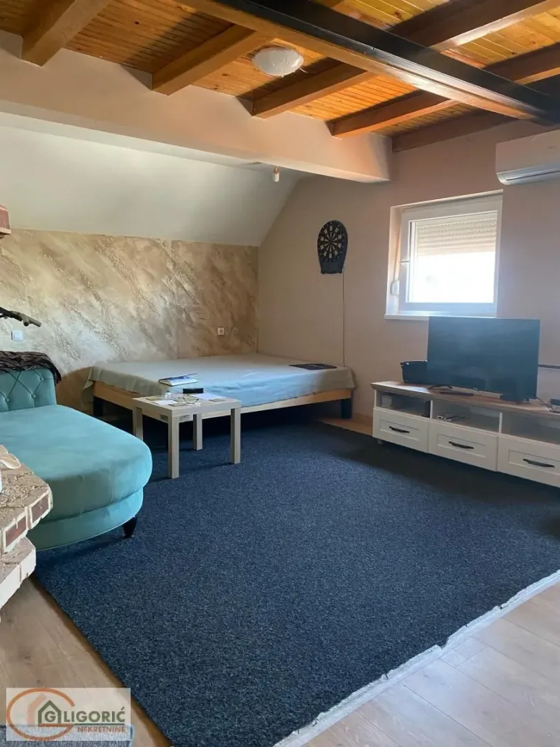 Attic space furnished with a bed, sofa, television, and a wooden ceiling.