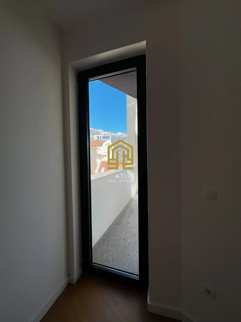Pogled kroz balkonska vrata na terasu i okolne zgrade.