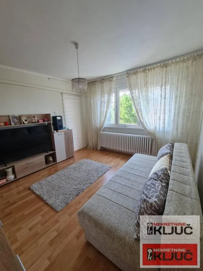 Dnevna soba sa garniturom za sedenje, televizorom i prozorom sa zavesama.
