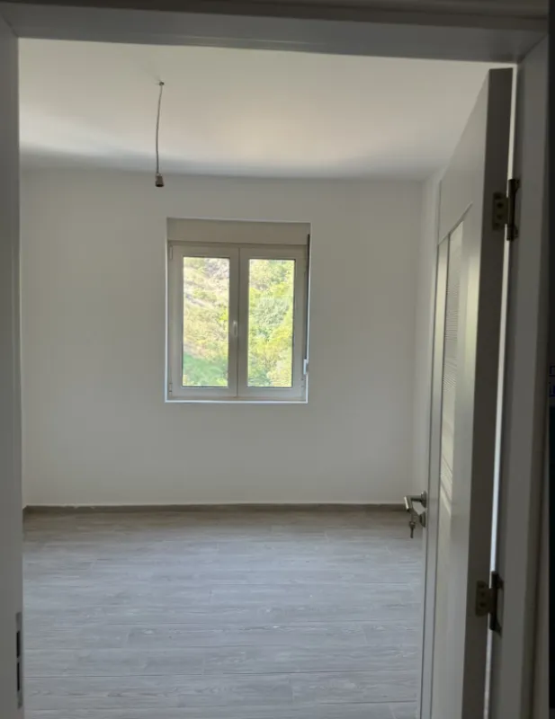 Pogled kroz vrata na praznu sobu sa bijelim zidovima i prozorom.