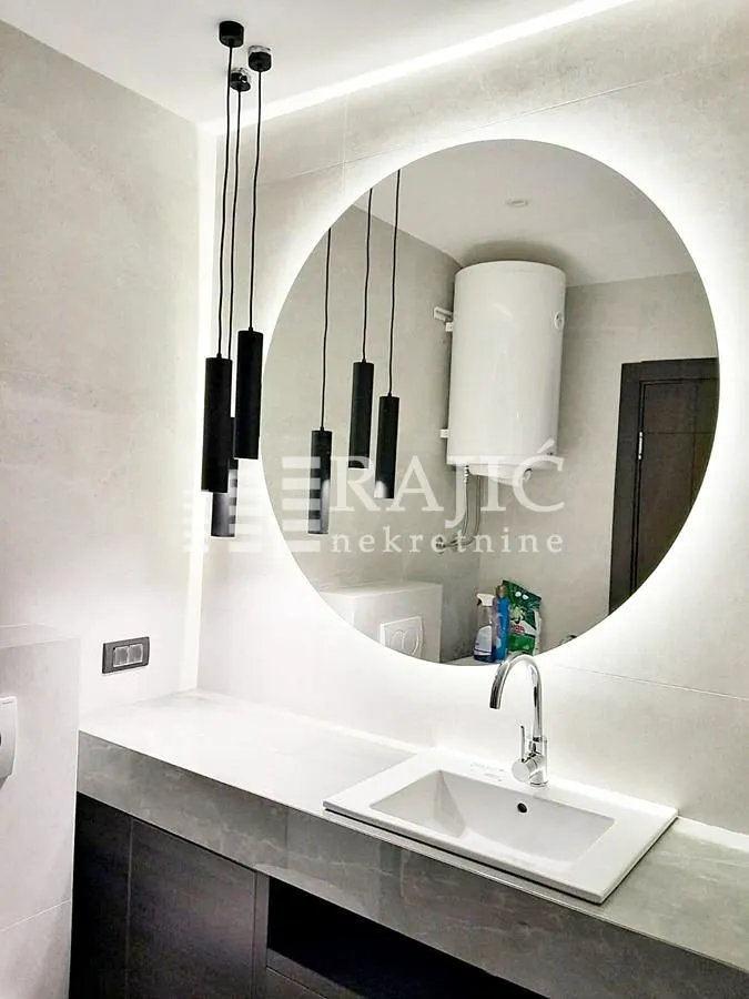 Modern bathroom with a sink, large round backlit mirror, and pendant lights.