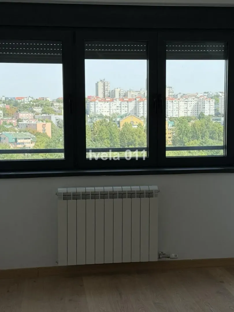 Pogled kroz prozor na gradsko naselje iz prostorije sa radijatorom.