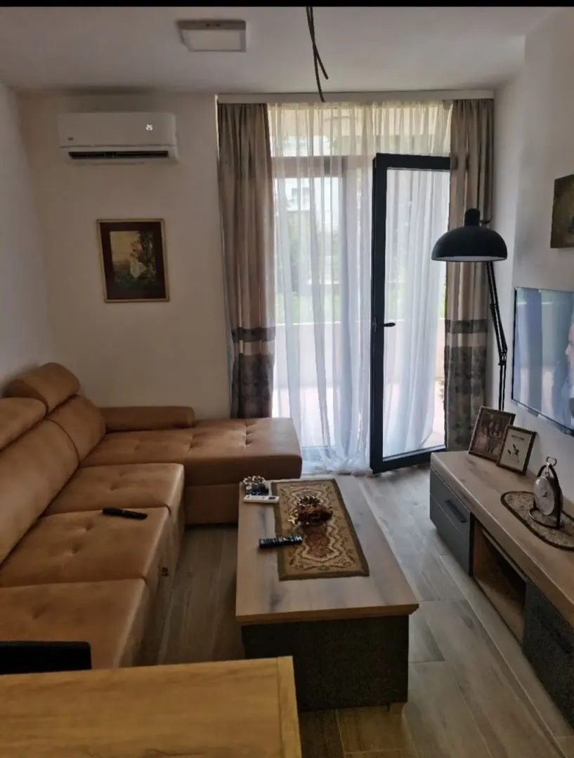 Dnevna soba sa ugaonom garniturom, stočićem i televizorom.