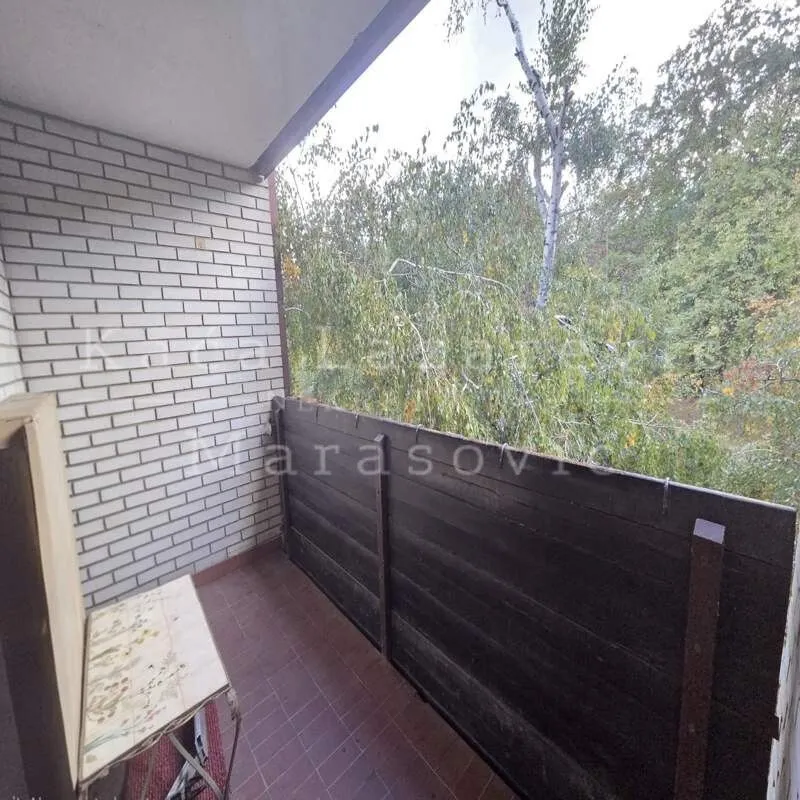 Natkriveni balkon sa drvenom ogradom i pogledom na zelenilo.