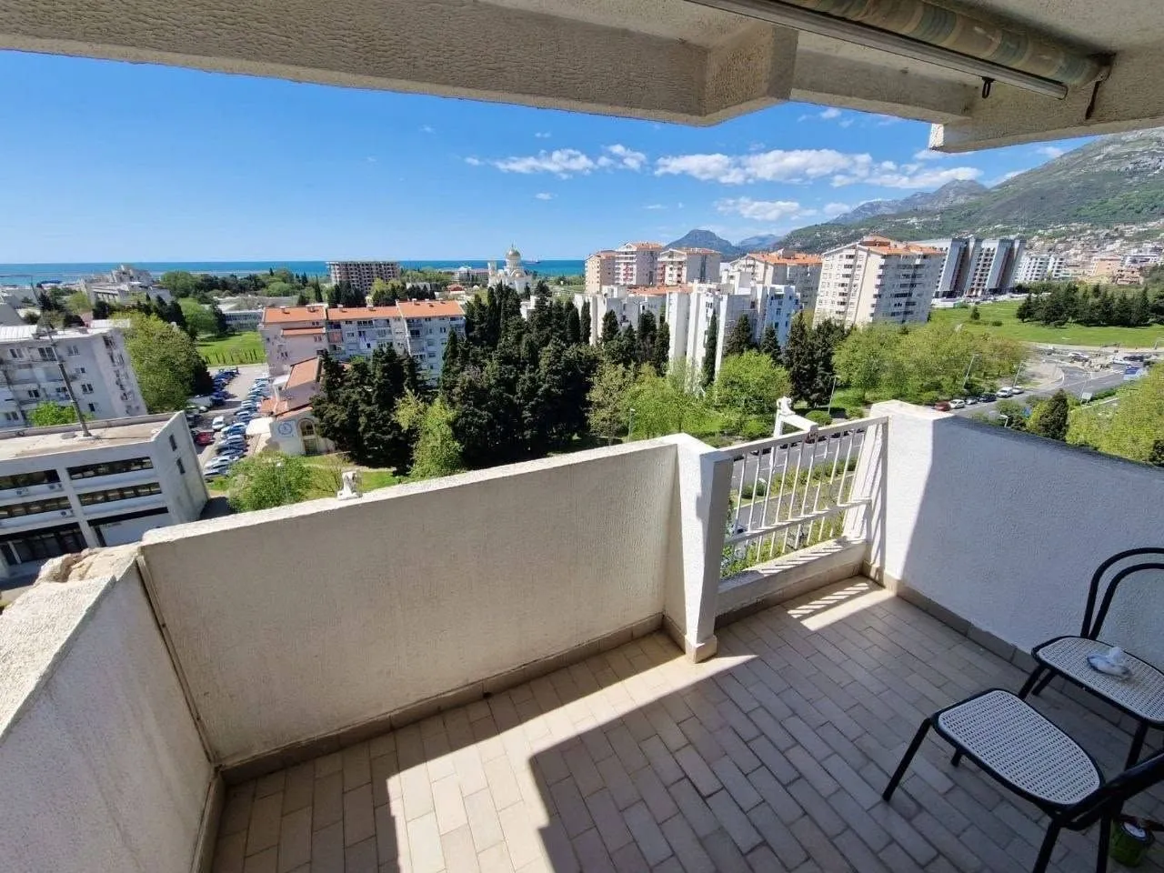 Spacious balcony with seating furniture and a view of the city and the sea.