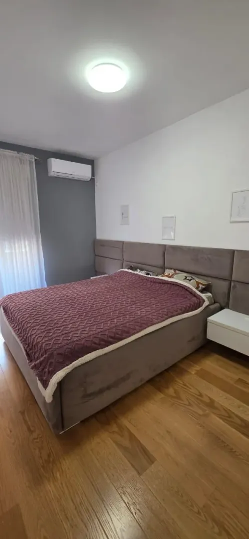 Spavaća soba sa bračnim krevetom, drvenim podom i klima uređajem.
