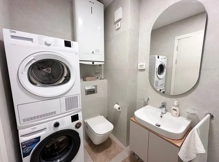 Bathroom equipped with a washbasin, toilet, and stacked washing and drying machines.