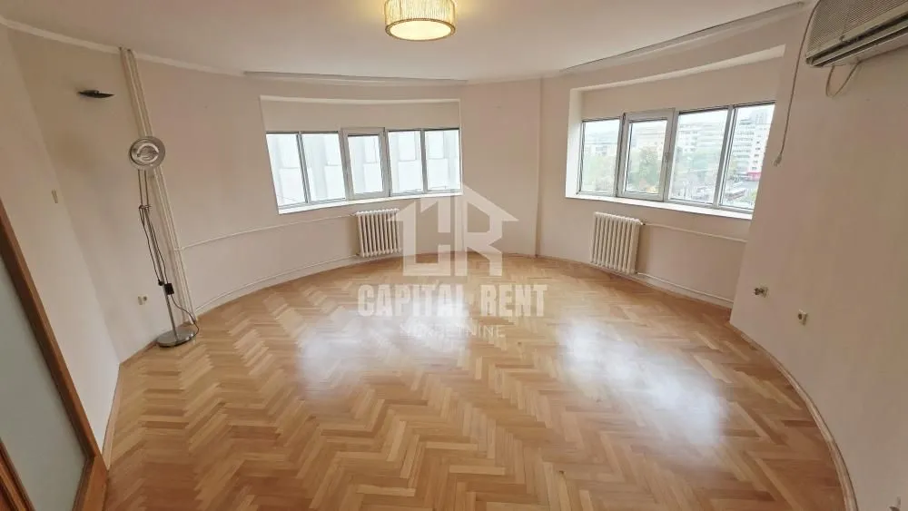 Empty living room with parquet flooring and large windows.