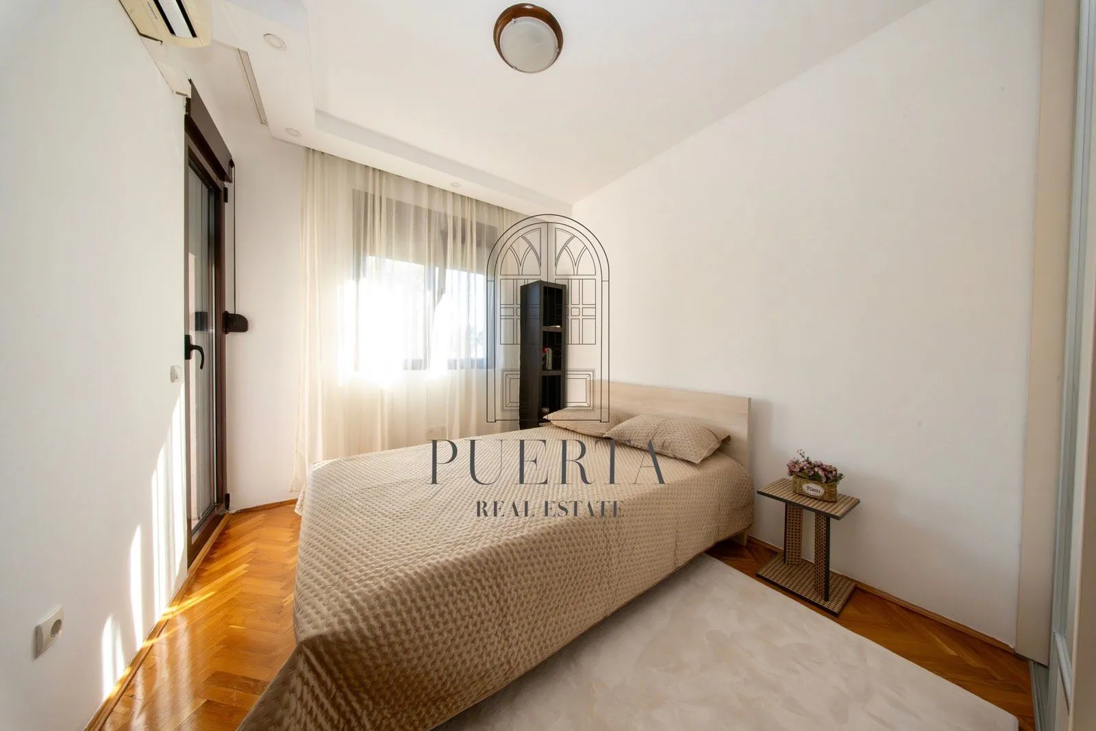 A furnished bedroom with a double bed and parquet flooring.