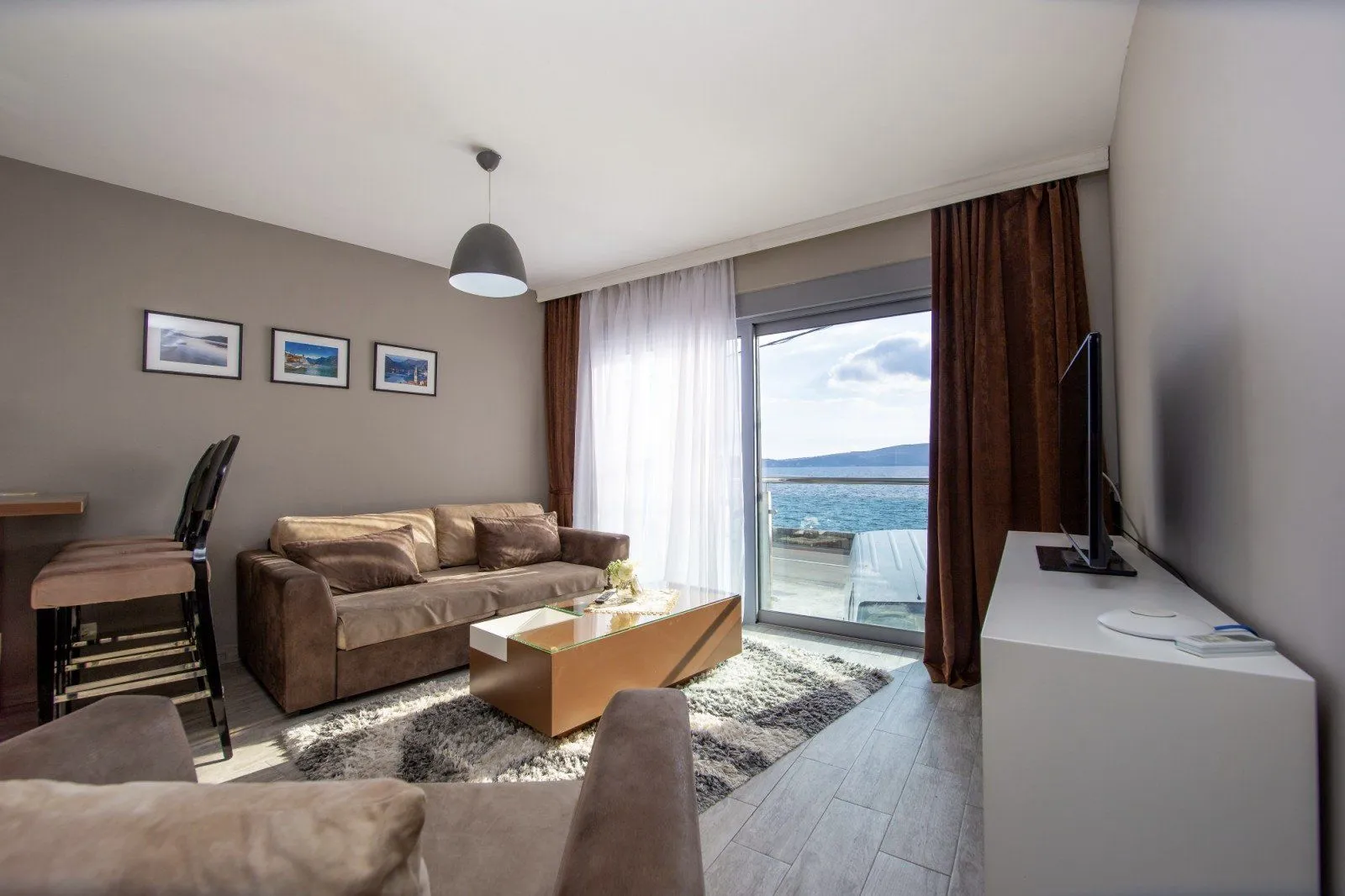 Living room with a sofa, TV, and a sea view through the balcony doors.
